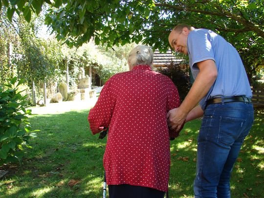 Seniorin und Pfleger gehen gemeinsam im Garten